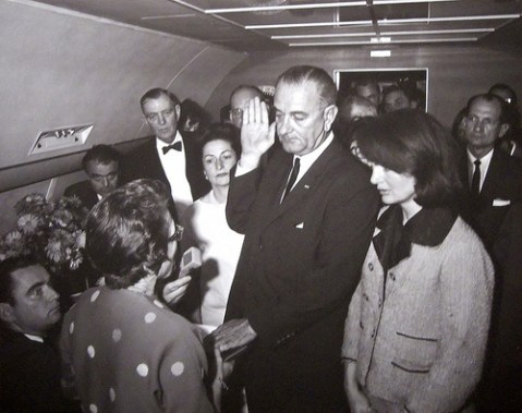 john_f_kennedy_assassination_lyndon_b_johnson_is_sworn_in_as_president_around_30_minutes_after_kennedy's_death;_either_side_of_him_is_the_new_and_previous_first_ladies_lady_bird_johnson_and_jackie_kennedy